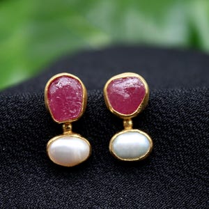 May include: A pair of gold earrings with pink and white stones. The earrings are made of gold and have a simple design.