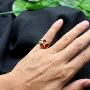 May include: A gold ring with three red gemstones. The ring is worn on a person's finger.