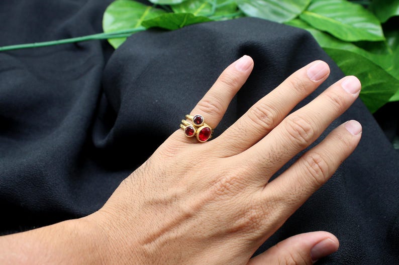 May include: A gold ring with three red gemstones. The ring is worn on a person's finger.
