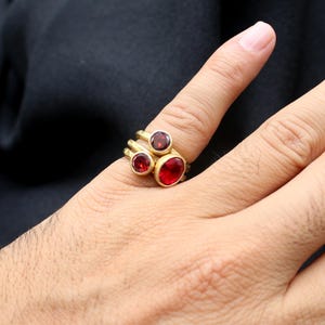 May include: A gold ring with three red gemstones. The ring is worn on a person's finger.