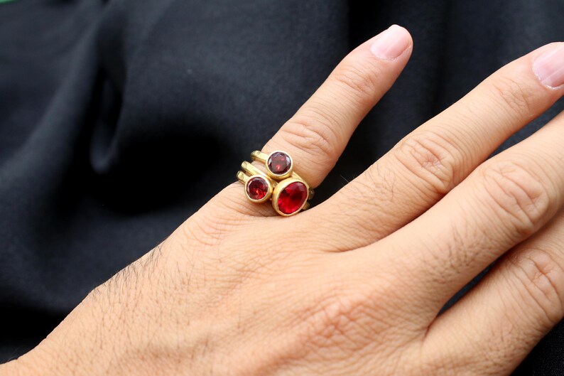 May include: A gold ring with three red gemstones. The ring is worn on a person's finger.