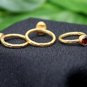 May include: Three gold rings with hammered textures. Two rings are plain and one ring has a red gemstone.