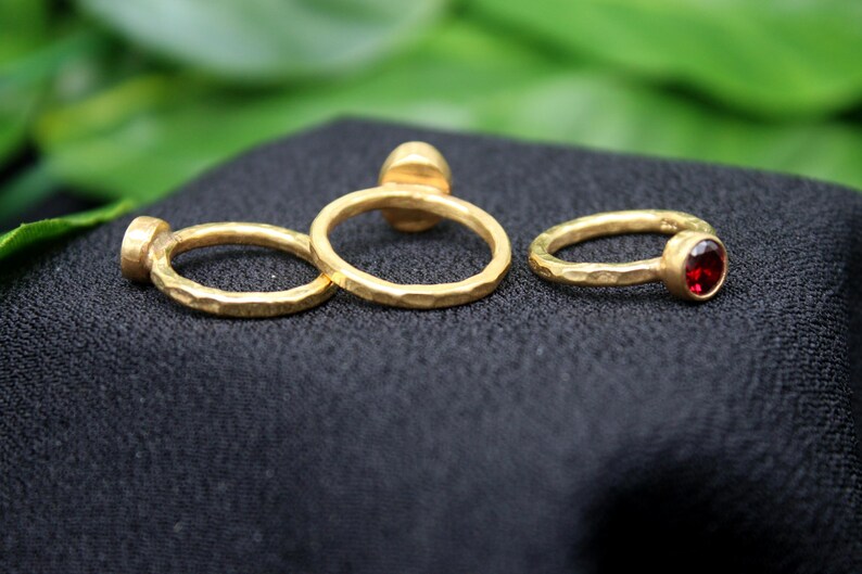 May include: Three gold rings with hammered textures. Two rings are plain and one ring has a red gemstone.