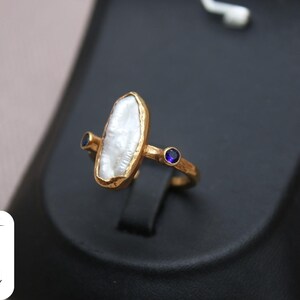 May include: Gold ring with a large, white, irregular shaped pearl and two small, blue gemstones.