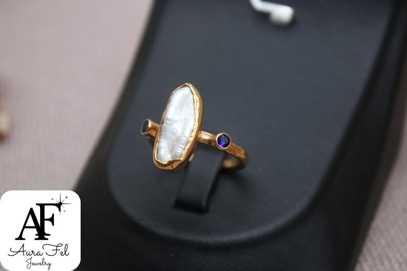 May include: Gold ring with a large, white, irregular shaped pearl and two small, blue gemstones.