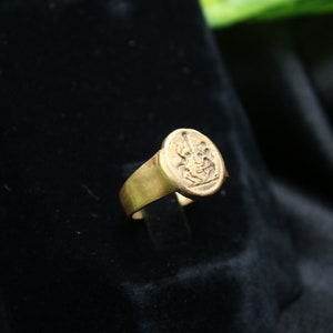 May include: A gold signet ring with a detailed engraved design. The ring has a rounded top and a smooth band.