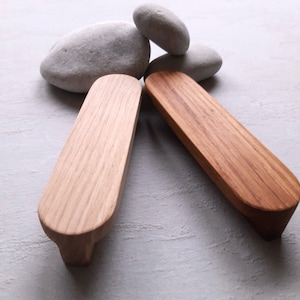 May include: Two wooden drawer pulls with a rounded rectangular shape. The pulls are made of light and dark wood.