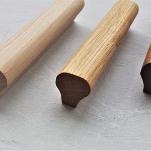 Peut inclure: Trois poignées de tiroir en bois avec une forme arrondie et incurvée. Les poignées sont en bois naturel et ont une finition brun clair, brun moyen et brun foncé.