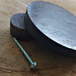 May include: Two dark wood circles, one smaller than the other, with a silver screw lying on a wooden surface.