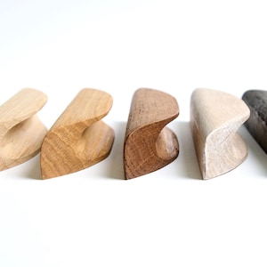 May include: Five wooden drawer pulls in different shades of brown, natural wood, and black. The pulls are all the same shape, with a curved top and a flat bottom.