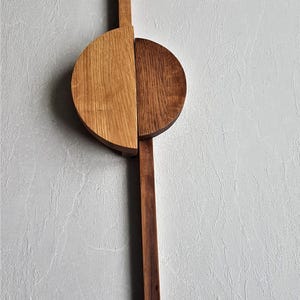 Peut inclure: Une horloge murale en bois avec un cadran circulaire divisé en deux. La moitié supérieure est en bois clair, tandis que la moitié inférieure est en bois foncé. Les aiguilles de l'horloge sont longues et fines, et le cadran est simple et minimaliste.