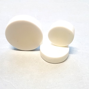 Puede incluir: Tres posavasos redondos de cerámica blanca de diferentes tamaños. El posavasos más grande está a la izquierda, el posavasos más pequeño está encima del posavasos del medio.