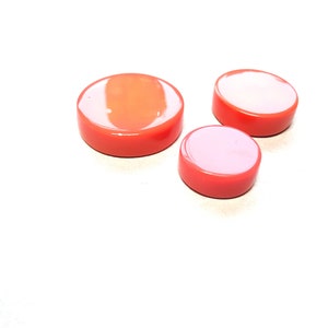 May include: Three round, orange-coloured, plastic game pieces. The pieces are different sizes, with the largest piece at the back and the smallest piece at the front.