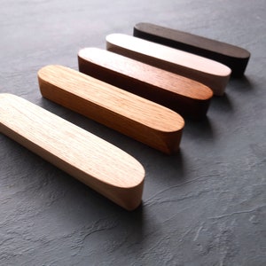 May include: Five wooden drawer pulls in various shades of brown, from light to dark, arranged in a row from lightest to darkest.