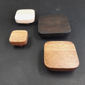 Può includere: Quattro sottobicchieri quadrati in legno in diverse tonalità di marrone, bianco e nero. I sottobicchieri sono in legno e hanno una finitura liscia.
