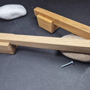 Può includere: Due maniglie per armadietti in legno marrone chiaro con un design a barra rettangolare e supporti angolati. Le maniglie presentano una texture naturale con venature del legno e sono accompagnate da due piccole viti in metallo argentato.