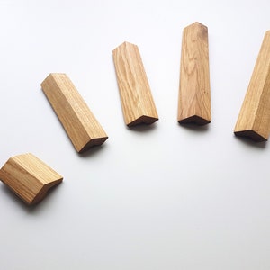 May include: Five wooden, geometric-shaped blocks with a natural wood grain finish. The blocks are arranged on a white surface, with one block separated from the others. The blocks have a light brown color.