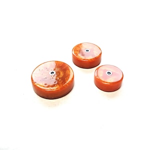 May include: Three round orange resin coasters with a small black dot in the center of each.
