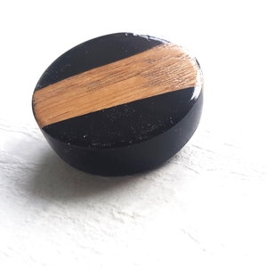 Könnte beinhalten: Ein runder Holz-Knopf mit einem schwarz-braunen Streifenmuster. Der Knopf ist aus Holz und hat eine glatte, polierte Oberfläche.