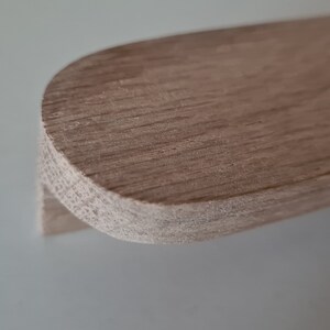 Puede incluir: Una manija de armario de madera marrón claro con un borde redondeado.