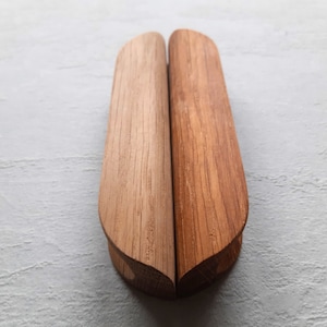 May include: Two wooden shoe trees, side by side, with a light and dark brown finish. The shoe trees have a curved, elongated shape, designed to maintain the shape of shoes. The wood grain is visible.