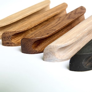 May include: Five wooden drawer pulls in various shades of brown, including natural, dark brown, and black. The pulls are all the same shape, with a curved, slightly rounded design.