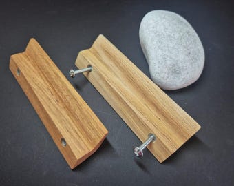 May include: Two rectangular light brown wooden drawer pulls with a beveled edge design. Each handle features two silver metal screws protruding from the back, and a smooth, natural wood grain finish is visible across the surface of both items.