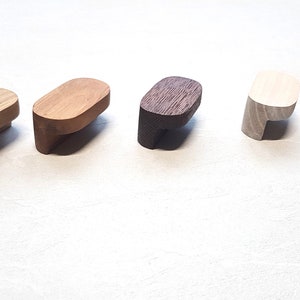Peut inclure: Cinq boutons de cabinet en bois dans différentes couleurs et finitions. Les boutons sont de forme ovale avec une légère courbe sur le dessous. Les couleurs sont bois naturel, bois clair, bois foncé, blanc et noir.
