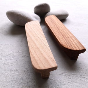 Può includere: Due maniglie per cassetti in legno con bordi arrotondati e una finitura in legno naturale. Le maniglie sono realizzate in legno massello e hanno un design semplice e moderno.