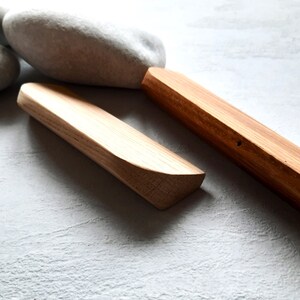 May include: Two wooden blocks, one long and one short, with rounded edges. The blocks are made of light brown wood and have a natural finish. The blocks are sitting on a white surface.