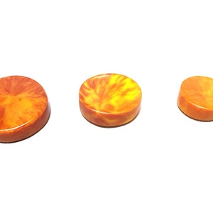 Può includere: Tre bottoni rotondi in resina, di colore arancione e giallo, con un motivo a spirale.