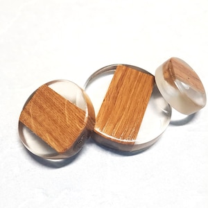 May include: Three round resin coasters with a wood inlay. The coasters are clear and have a light brown wood inlay.