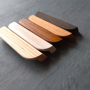 Könnte beinhalten: Sechs Holz-Schubladengriffe in verschiedenen Brauntönen, von hell bis dunkel, mit abgerundeten Kanten.