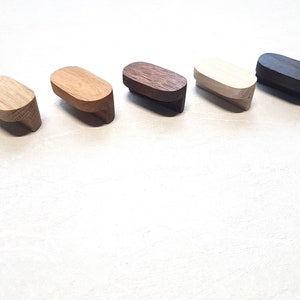 May include: Five wooden cabinet knobs in various shades of brown, beige, and black. The knobs are oval shaped and have a slightly curved design.