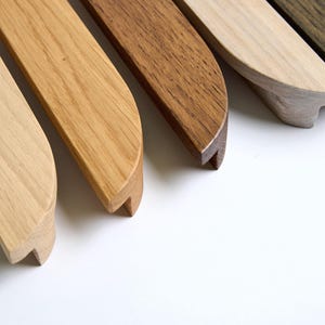 Può includere: Cinque maniglie per armadi in legno in diverse tonalità di marrone, dal chiaro al scuro. Ogni maniglia ha una forma arrotondata, leggermente curva.
