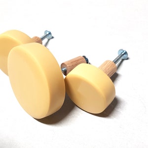 Op de afbeelding: Drie ronde, gele kastknoppen met houten basis en zilveren schroeven.