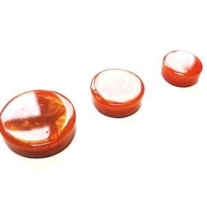 May include: Three round, orange resin coasters with a white, glittery finish.