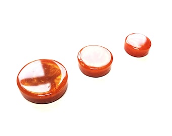 May include: Three round, orange resin coasters with a white, glittery finish.