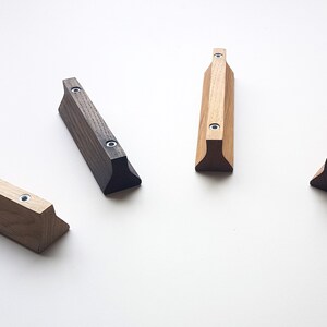 May include: Four wooden cabinet pulls in different wood stains. The pulls are all the same shape, with a rectangular body and a triangular base. The pulls are arranged in a row, with the darkest stain on the left and the lightest stain on the right.
