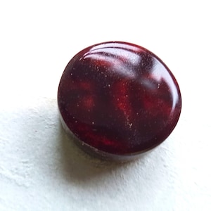May include: A dark red oval-shaped cabochon gemstone with a marbled pattern and a glossy finish.