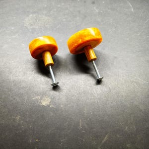 Può includere: Due pomelli rotondi per mobili con parte superiore in resina arancione traslucida e motivi marmorizzati. Ogni pomello presenta una base cilindrica in legno fissata a una vite in metallo color argento, come componente funzionale per cassetti.