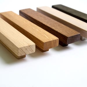 Könnte beinhalten: Sechs Holzknaufgriffe in verschiedenen Brauntönen, von hell bis dunkel. Die Griffe sind rechteckig und haben eine leicht abgerundete Kante.