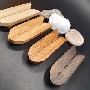 May include: Five wooden drawer pulls in various shades of brown, from light to dark. The pulls are shaped like a teardrop and are made of two pieces of wood joined together.
