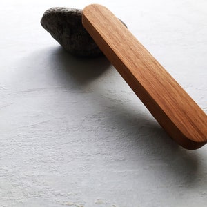 May include: A long, rectangular wooden handle with rounded edges. The handle is made of light brown wood and has a smooth finish.