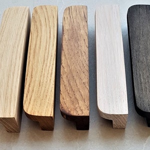 Puede incluir: Cinco tiradores de cajón de madera en diferentes acabados. Los tiradores son todos del mismo tamaño y forma, pero tienen diferentes manchas. Los acabados incluyen natural, marrón claro, marrón oscuro, blanco y negro.