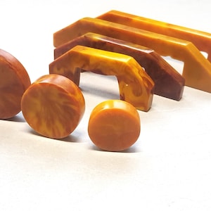 Puede incluir: Un juego de siete tiradores de cajones de baquelita vintage en varias formas y tamaños. Los tiradores son de color marrón y amarillo moteado.