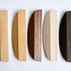 May include: Five wooden half-circle shapes in different shades of brown, from light to dark. The shapes are arranged horizontally, with the lightest shade on the left and the darkest shade on the right.