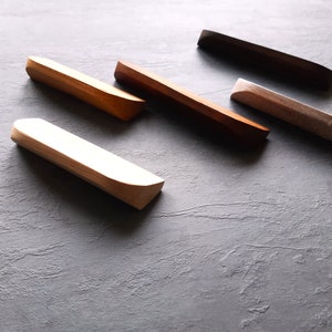 May include: Five wooden drawer pulls in various shades of brown, gray, and white. The pulls are all rectangular with rounded edges.