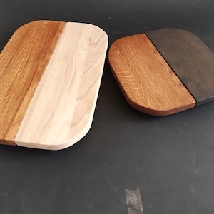 May include: Two wooden cutting boards, one oval and one square, with a light wood and dark wood finish. The boards are made of two different types of wood, creating a unique and stylish design.
