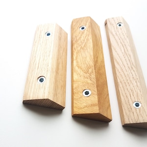 Puede incluir: Tres ganchos de pared de madera con forma triangular y acabado marrón claro. Cada gancho tiene dos tornillos plateados.